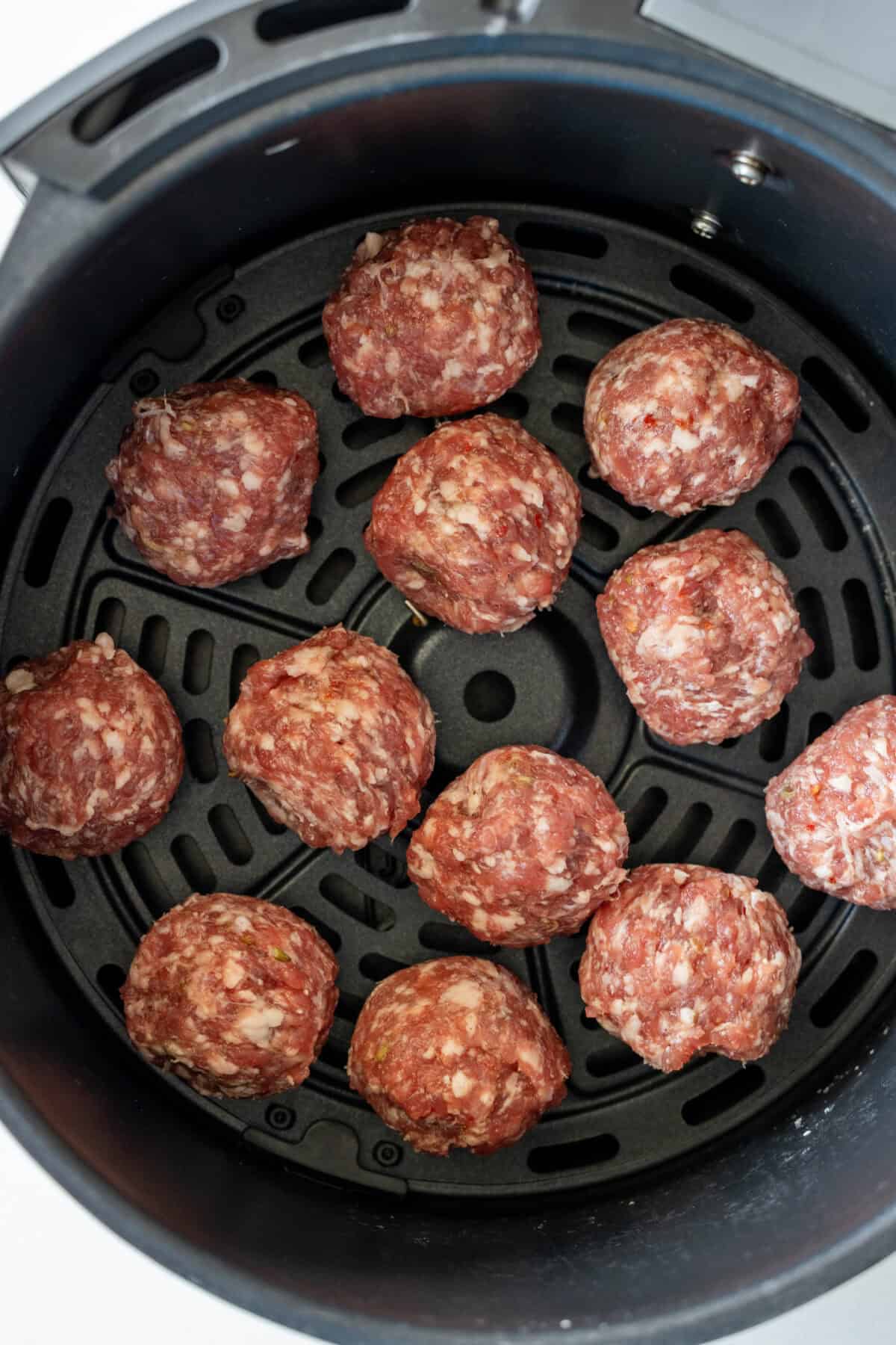 Raw keto meatballs recipe arranged in the basket of an air fryer.