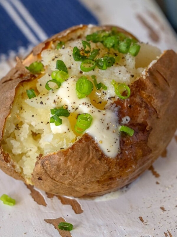 picture of baked potato with a pat of butter and chives on a wood cutting board