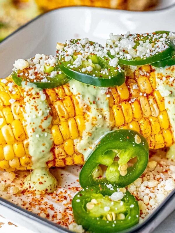 picture of elotes corn cob with crema, cheese, jalapenos, and spices on top