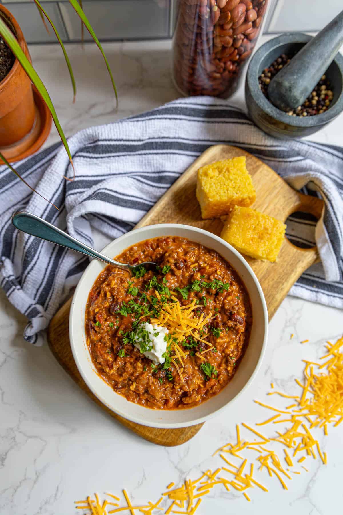 A bowl of chili on a wooden cutting board.