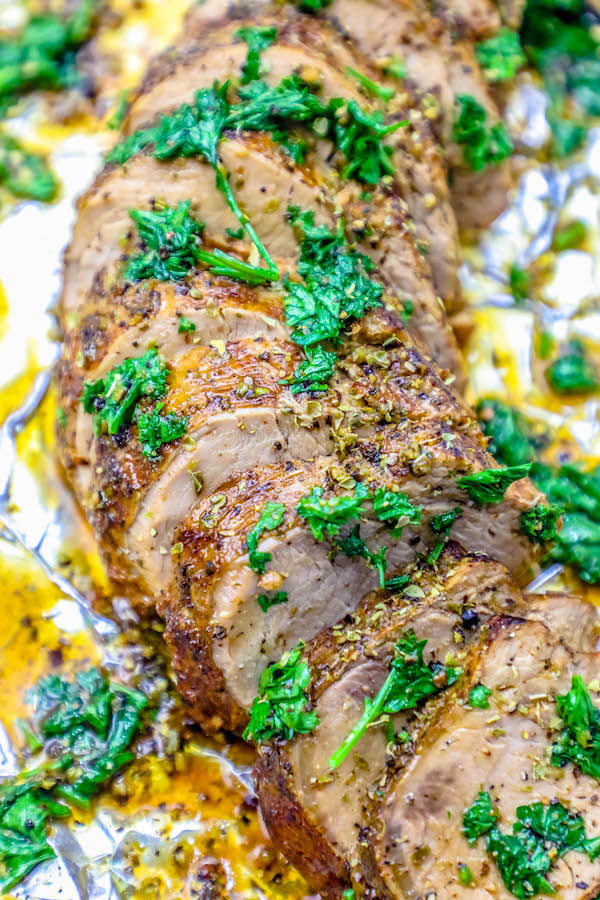 baked garlic pork tenderloin sliced and garnished with parsley on tinfoil. 