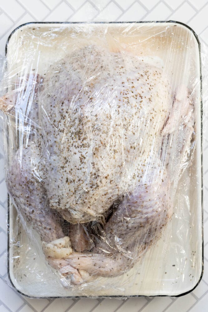 picture of turkey dry brining in plastic wrap on a white tray 