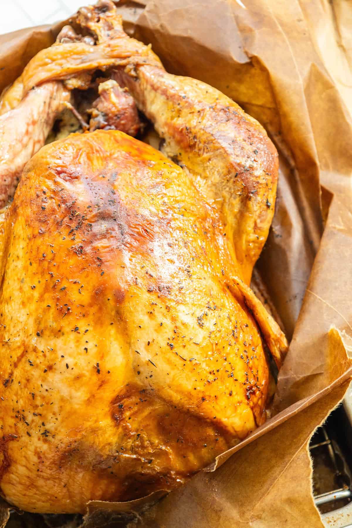 A roasted turkey with crispy, golden-brown skin lies on brown parchment paper, showcasing the simple elegance of a Brown Bag Herb Roasted Turkey Recipe.