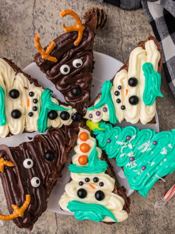 picture of brownies frosted to look like snowmen, christmas trees, and reindeer on a plate on a table