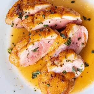 sliced duck breast with crispy skin and orange sauce spooned on top