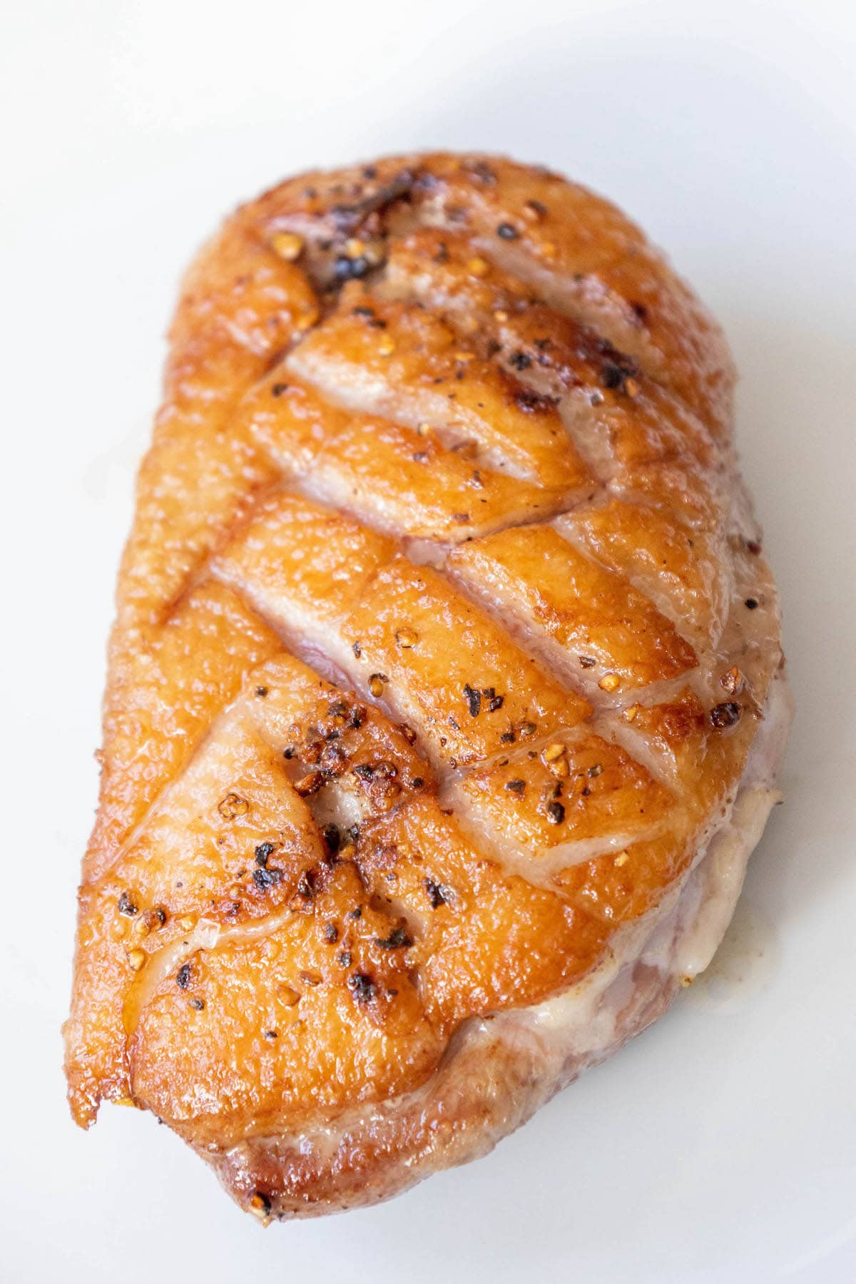 sliced duck breast with crispy fat seasoned with salt, pepper, and herbs topped with an orange sauce on a plate