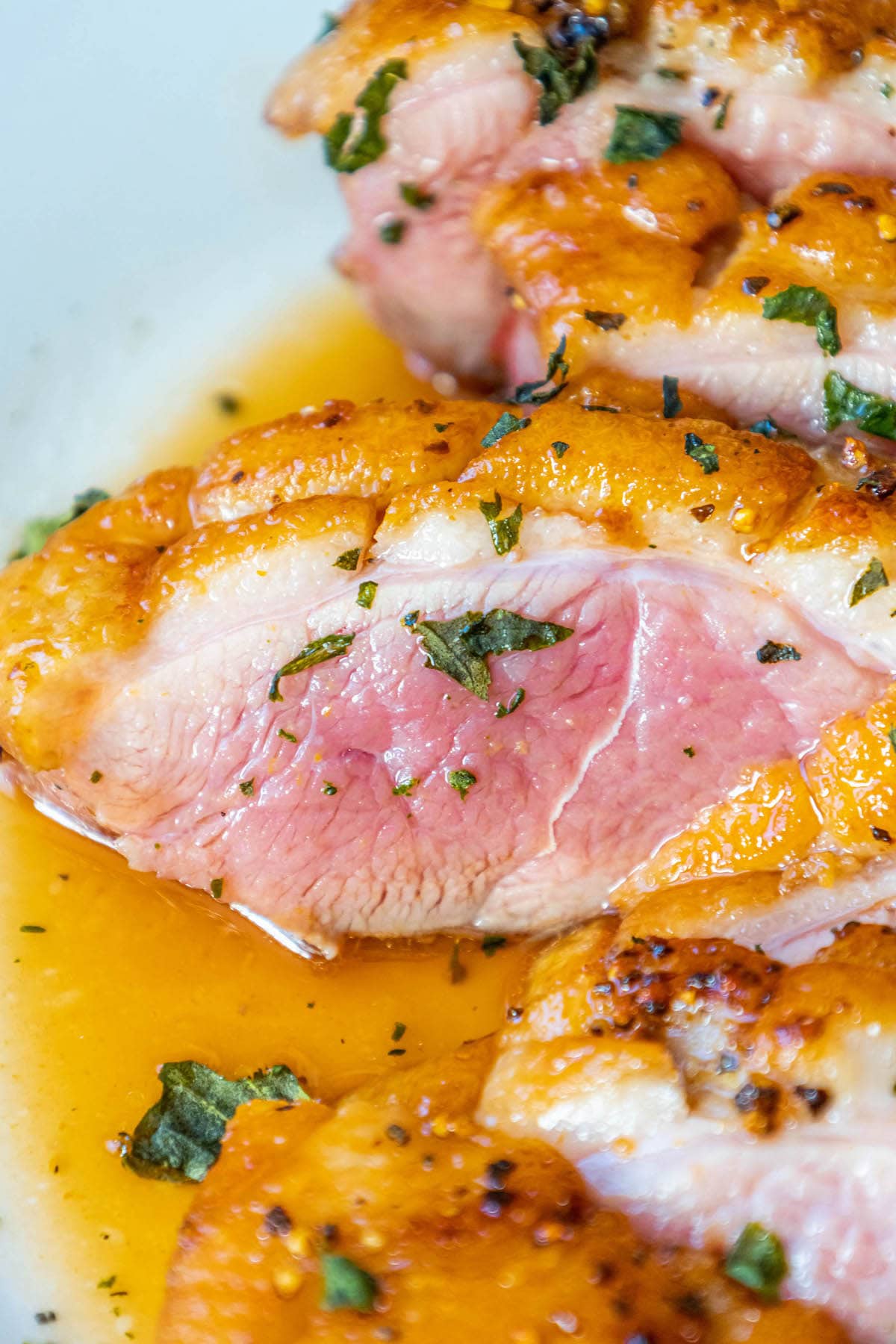 sliced duck breast with crispy fat seasoned with salt, pepper, and herbs topped with an orange sauce on a plate