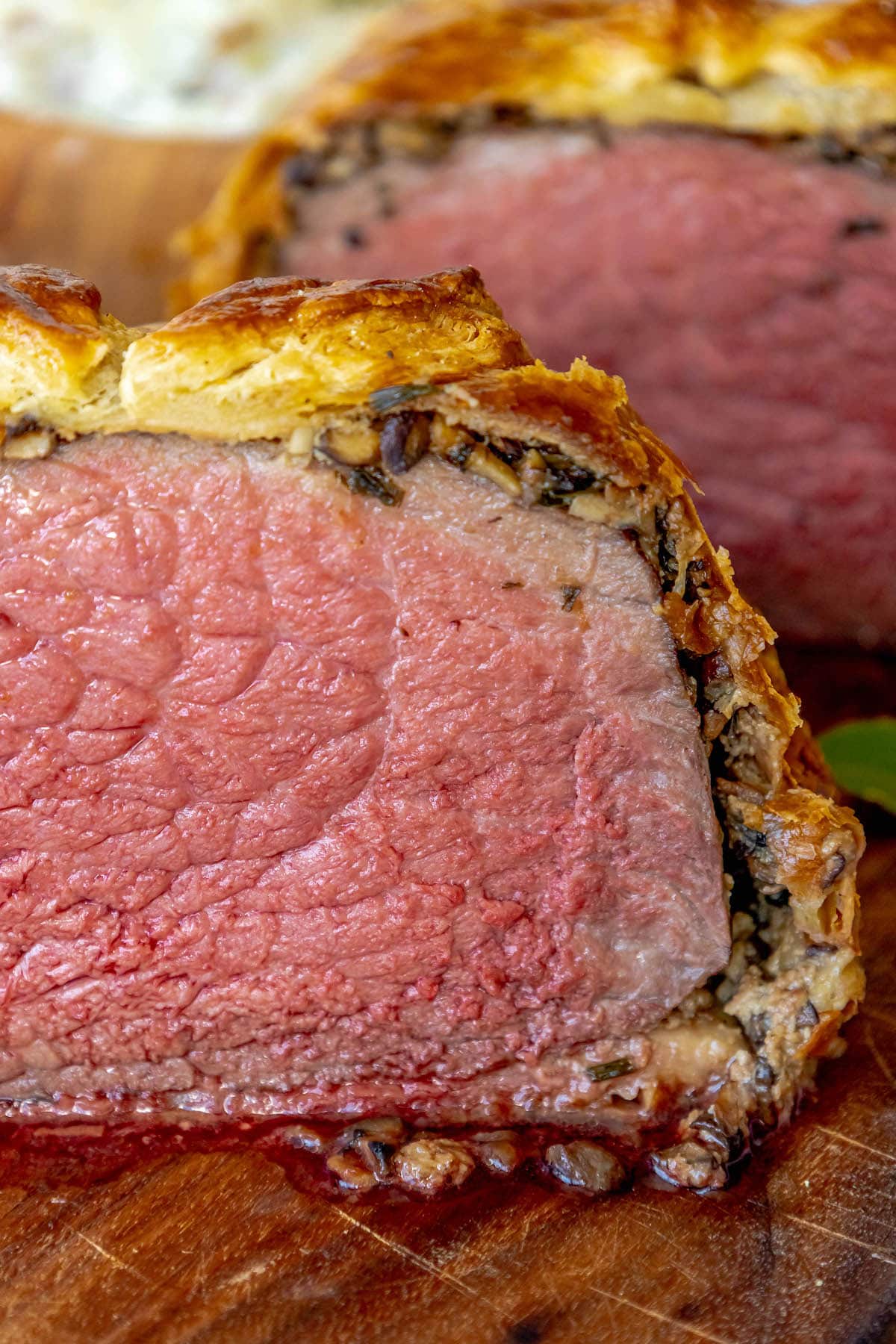 beef wellington cut in half wrapped in puff pastry with mushroom duxelle and pate on a wooden cutting board