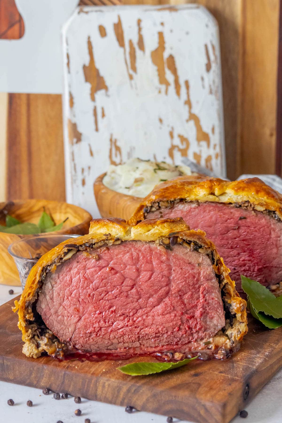 beef wellington wrapped in puff pastry sliced in half sitting on a cutting board with bay leaves