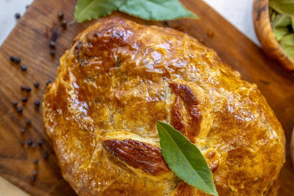 baked beef wellington on a wooden cutting board wit a bay leaf on top 