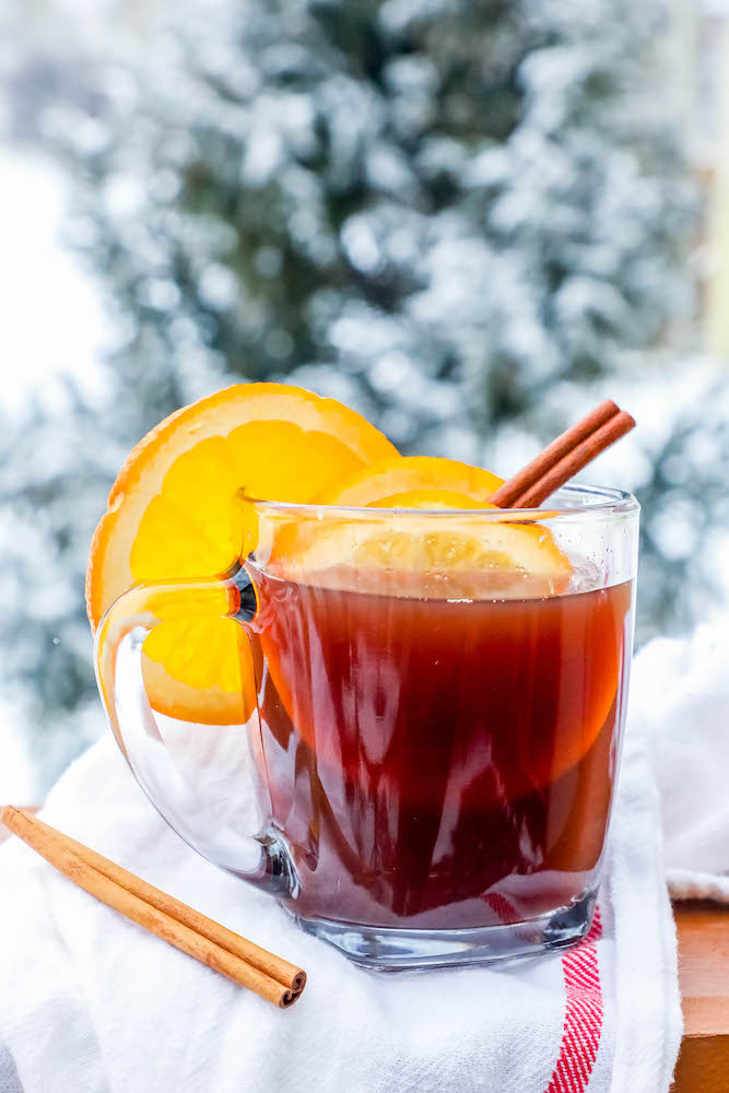 cider in a clear mug with slices of orange and cranberries with cinnamon sticks