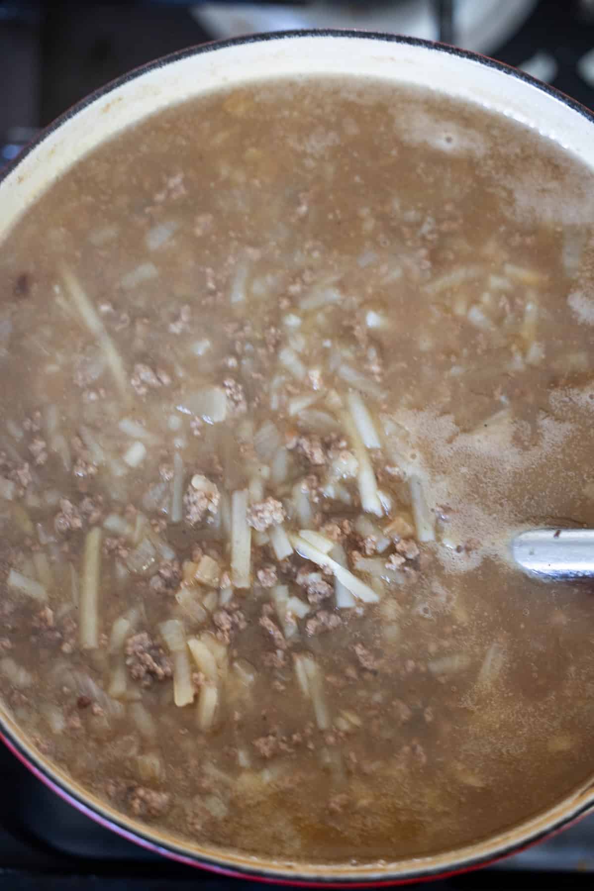 A pot of creamy hash brown hamburger soup with ground meat, onions, and noodles simmering.