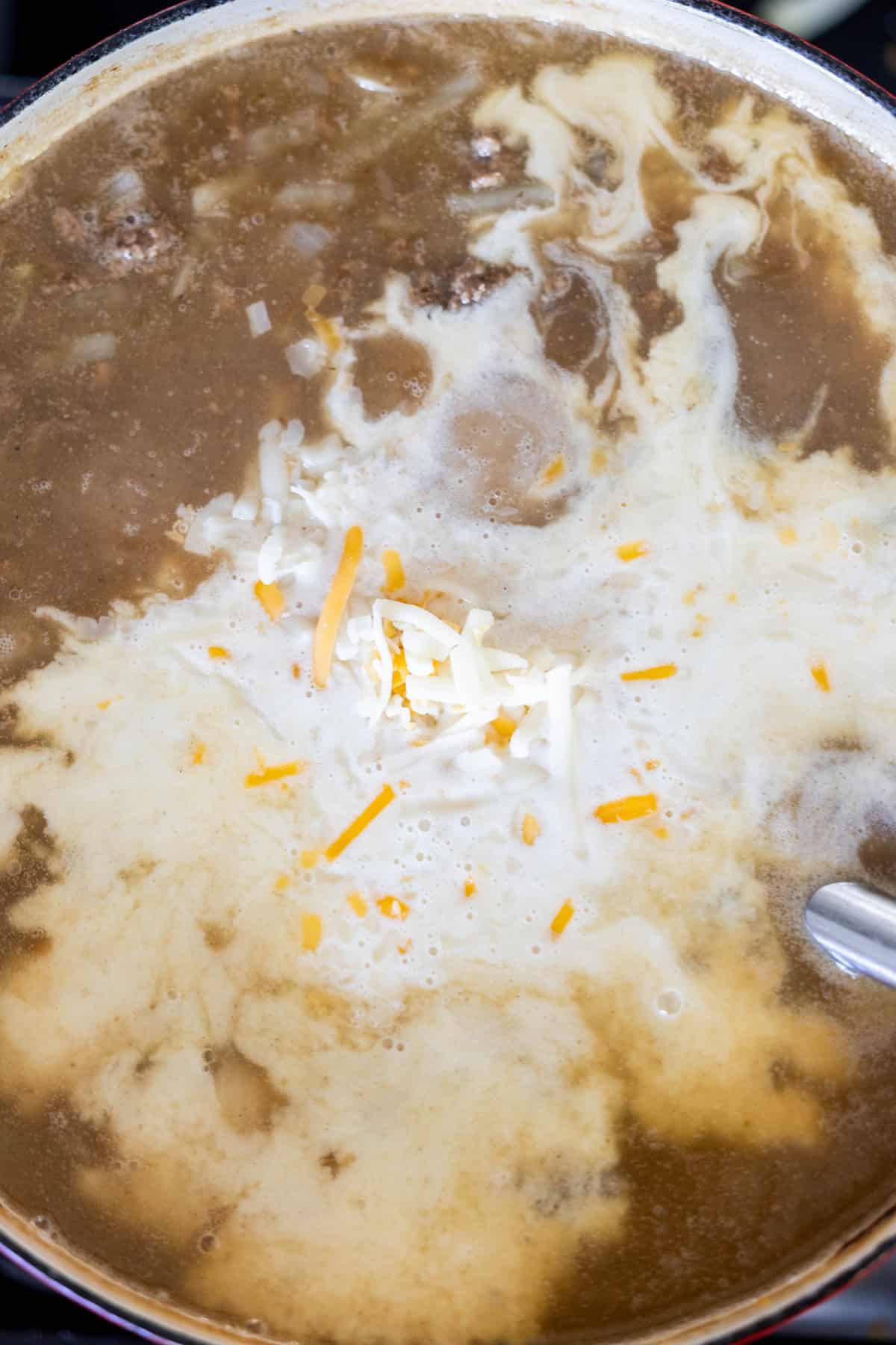 A pot of creamy hash brown soup with hamburger and cheese melting on top.