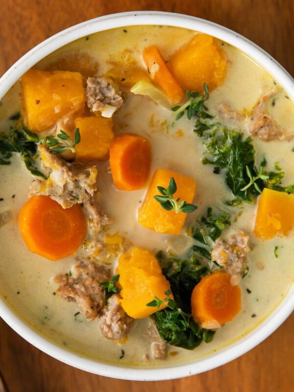 creamy turkey and butternut squash chili with carrots, thyme,, kale and peppers in a white bowl on a table