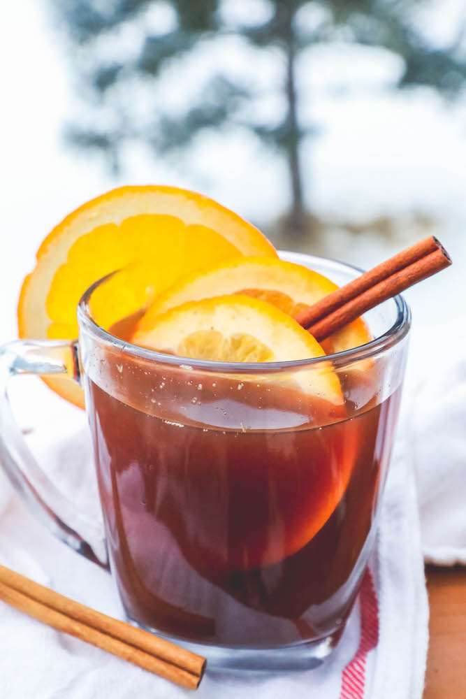 cider in a clear mug with slices of orange and cranberries with cinnamon sticks