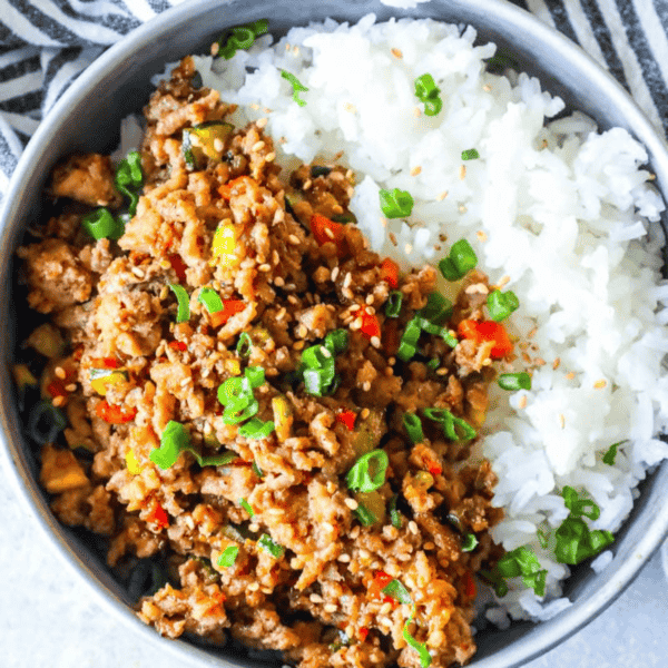A bowl containing white rice and spicy Mongolian ground turkey garnished with green onions.